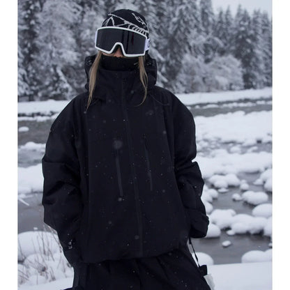 Model wearing the black version of the oversized hooded jacket, hands in pockets, beside a snowy river. 2