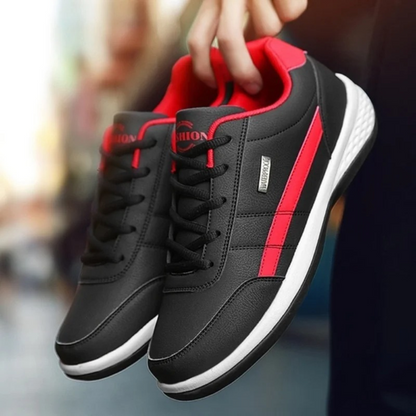 Pair of black faux-leather sneakers with red side stripe and red collar, held up by the heel against a blurred street. 1