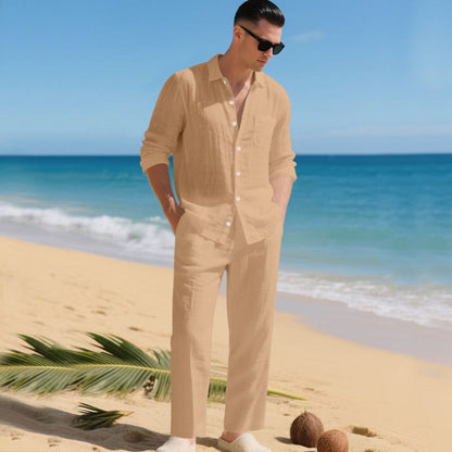 Man in sunglasses on a sandy beach wearing the sand-coloured long-sleeved shirt and matching straight trousers, hands in pockets. 5
