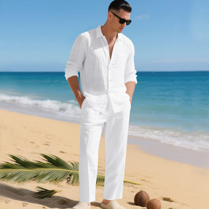 Man in sunglasses on a sandy beach wearing the white long-sleeved shirt and matching straight trousers, hands in pockets. 8