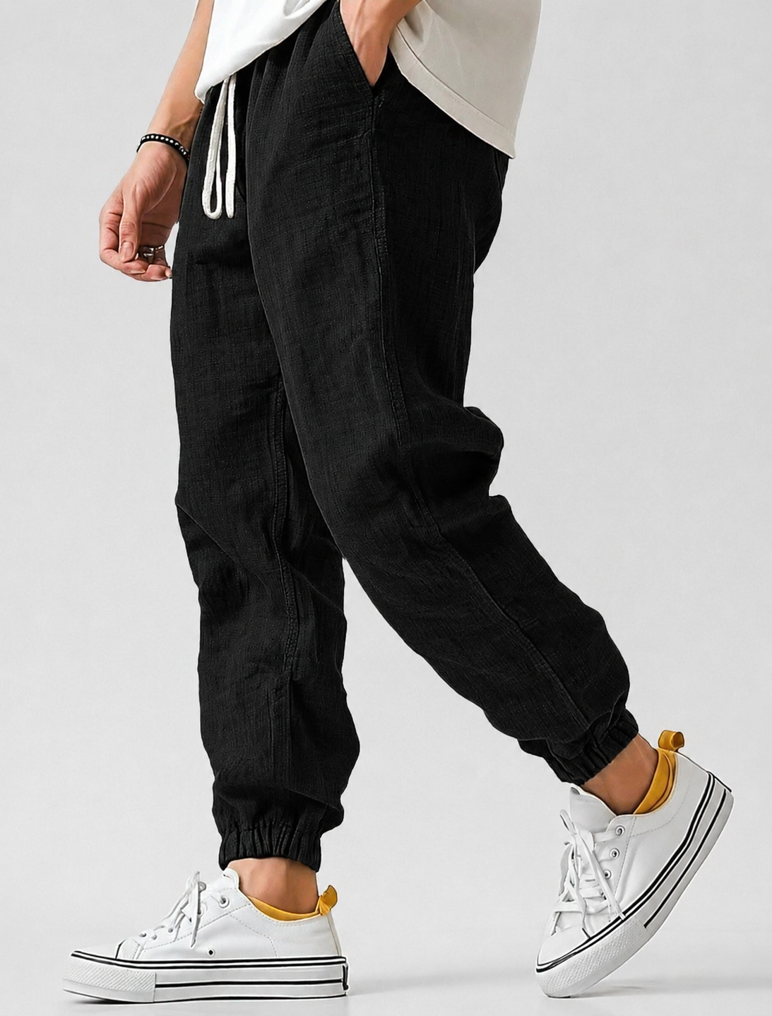 Black version of the jogger trousers on a model mid-stride, showing the drawstring waist, side pocket and elasticated hems. 3