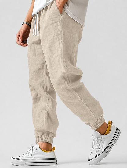 Pale beige jogger trousers worn by a model with hand in pocket, textured fabric, drawstring waist and cuffed ankles. 4