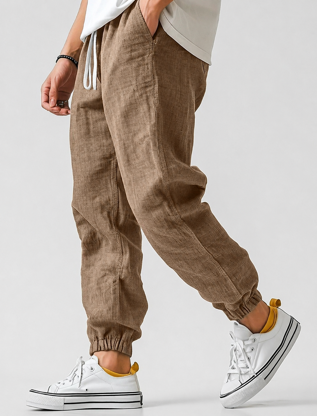 Model wearing the joggers in a warm tan-brown, showing the woven texture, white drawstring and elasticated ankle cuffs. 5
