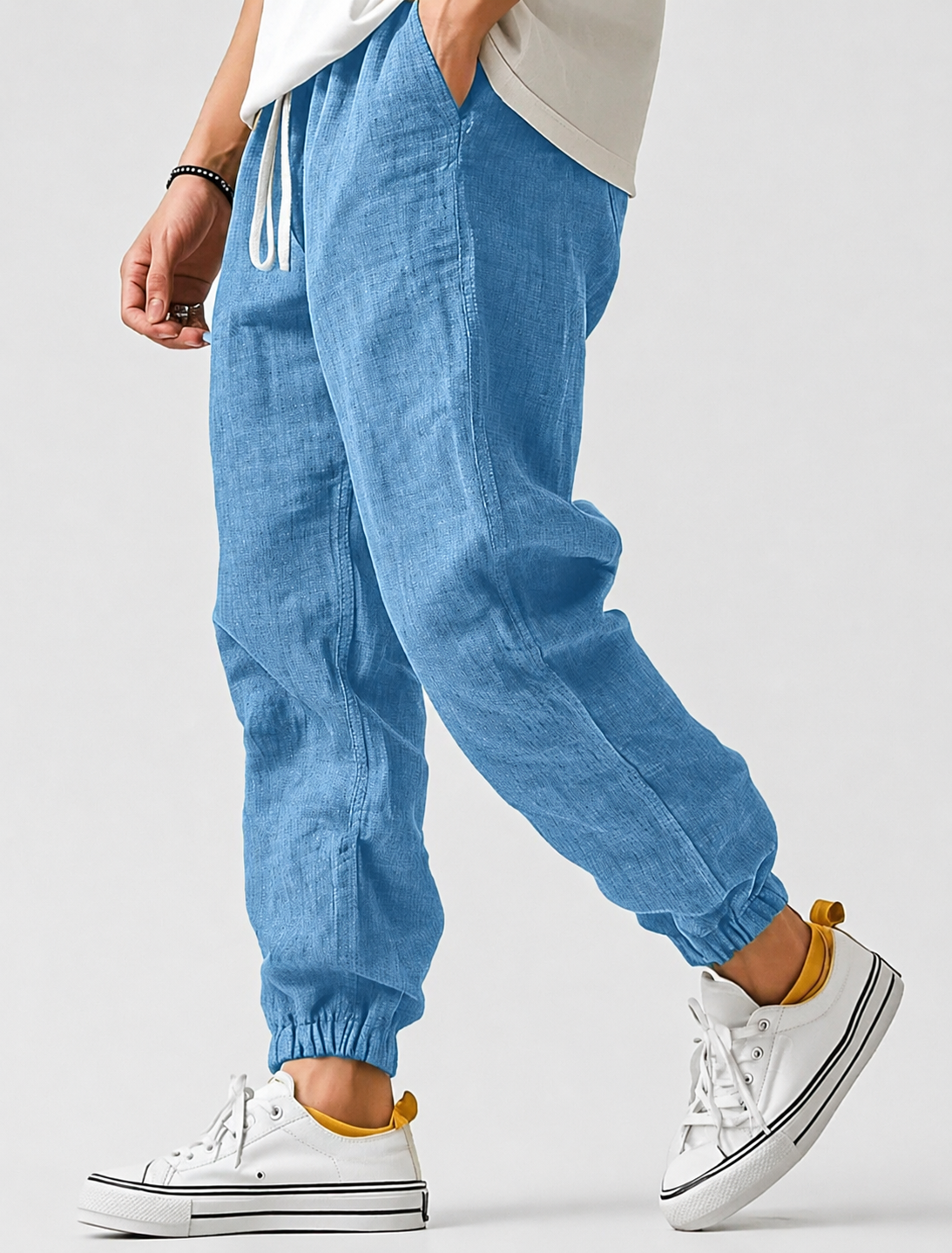 Model walking in light blue textured joggers with drawstring waist and elasticated ankle cuffs, worn with white trainers and a cream T-shirt. 1