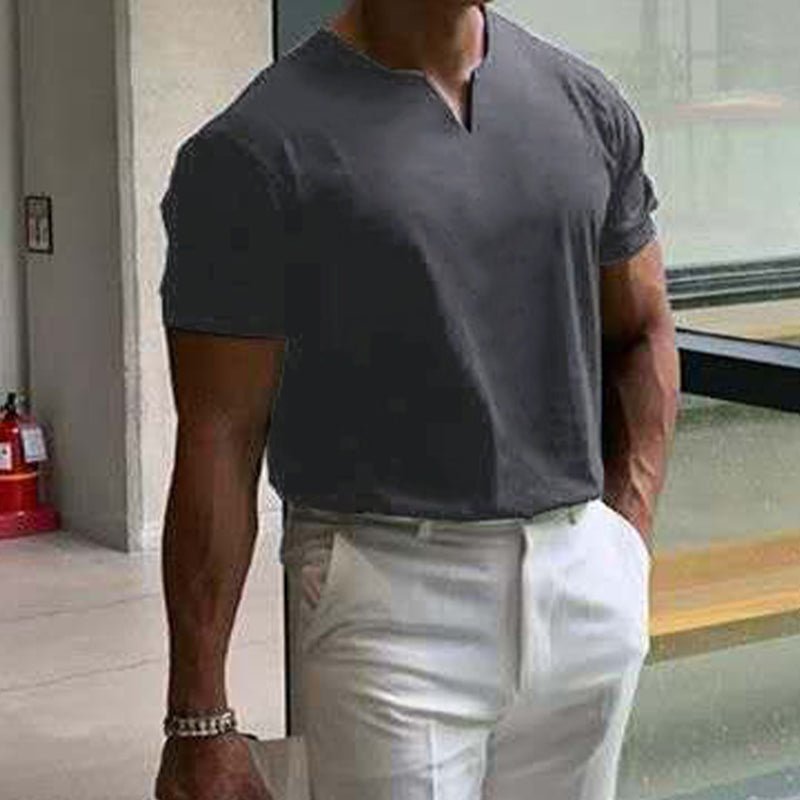 Dark grey V-neck tee worn with white trousers, model walking indoors with one hand in his pocket. 5