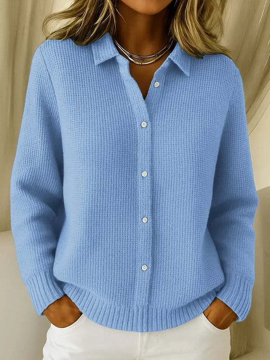 Model wearing the waffle-knit collared jumper in light blue, buttoned down the front, with hands in the pockets of white trousers. 1