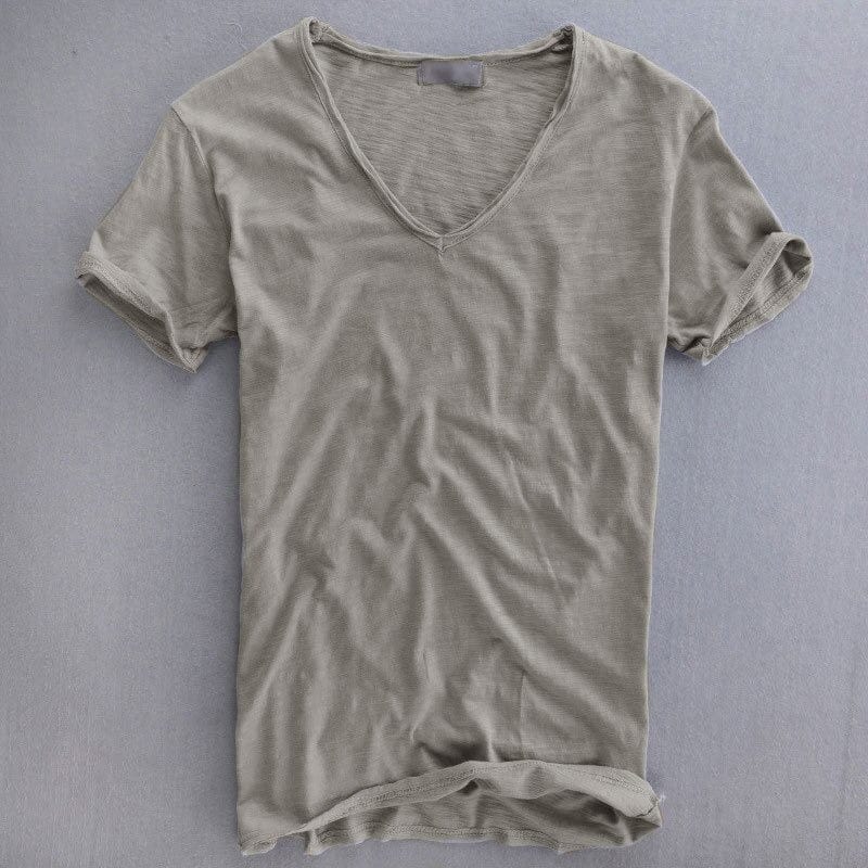 Short-sleeved V-neck t-shirt in light grey laid flat on a grey surface, showing the textured fabric and rolled sleeve cuffs. 1