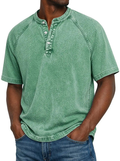 Closer, taller crop of a man in the washed green raglan Henley with button placket, hands in jeans pockets. 15