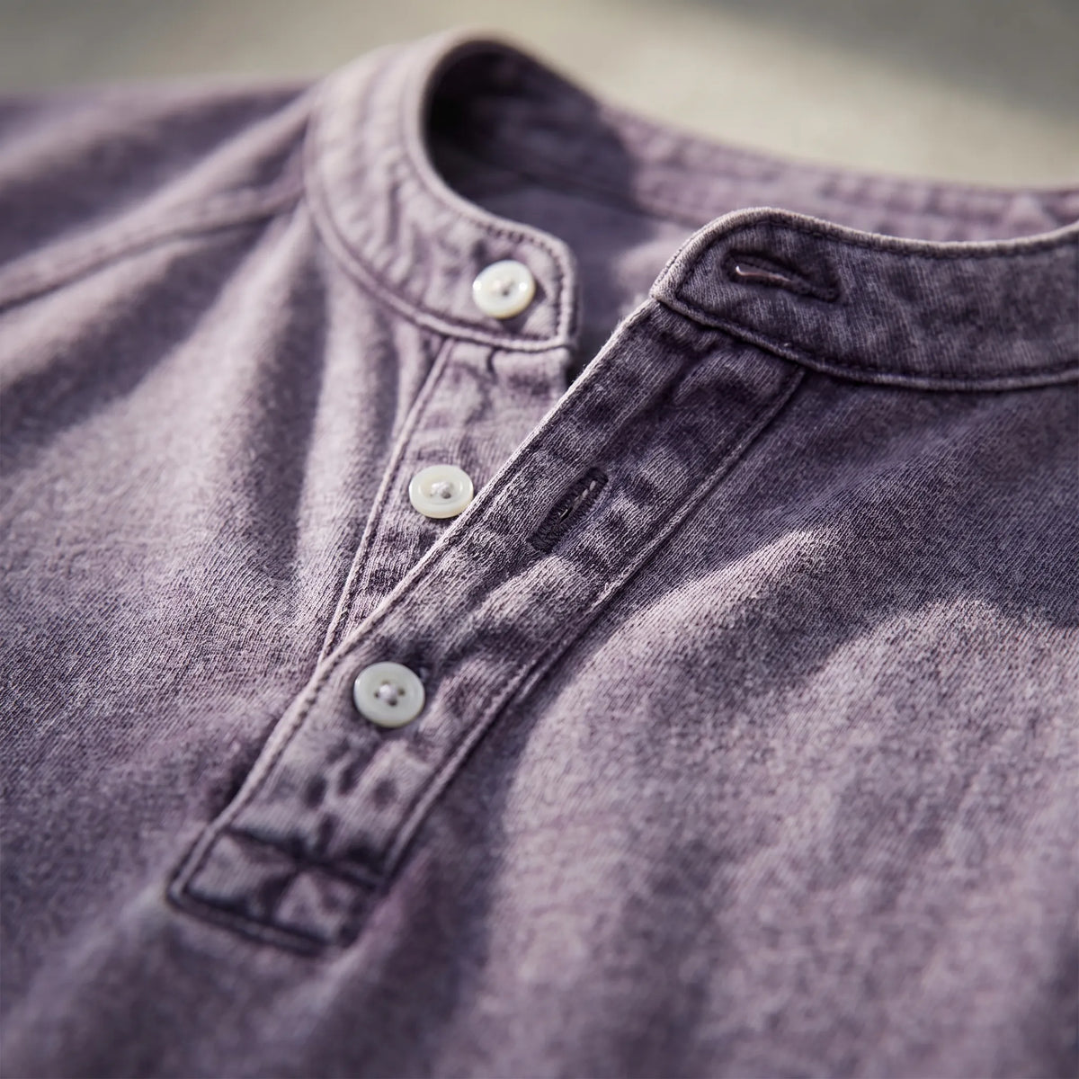 Close-up of the Henley placket and collar in mottled purple, showing pale buttons, a buttonhole and contrast stitching. 3