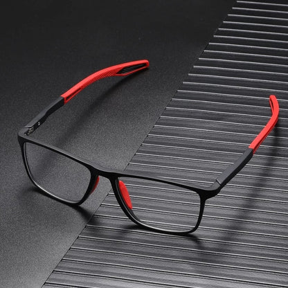 Black square-framed glasses with red arm tips and nose pads, resting on a dark ridged surface. 2