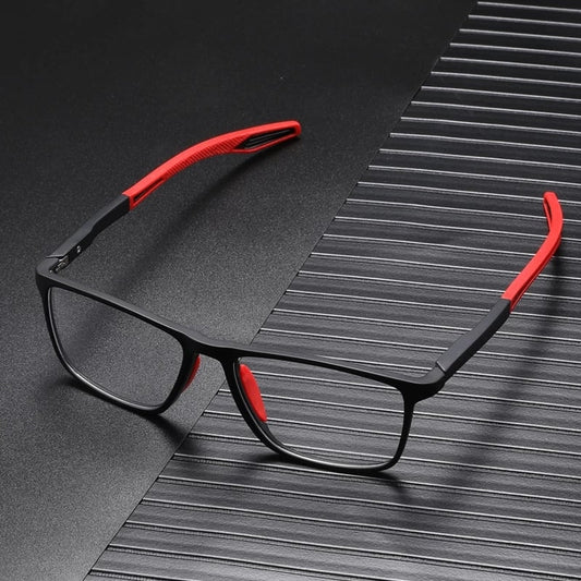 Black square-framed glasses with red arm tips and nose pads, resting on a dark ridged surface. 2