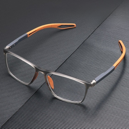 Translucent grey square glasses with orange arm tips and nose pads, resting on a dark textured surface. 3