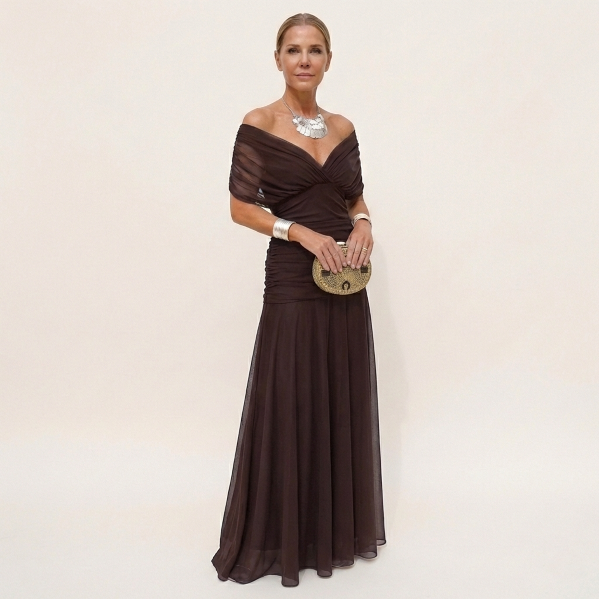 Full-length view of a dark brown chiffon version worn off the shoulder, with a ruched bodice and flowing skirt. 2