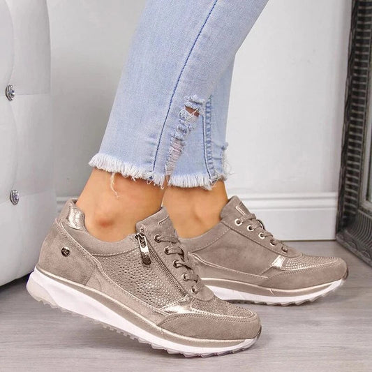 Side view of lace-up trainers in a taupe-beige suede finish with a side zip, worn with ripped light-blue jeans. 1