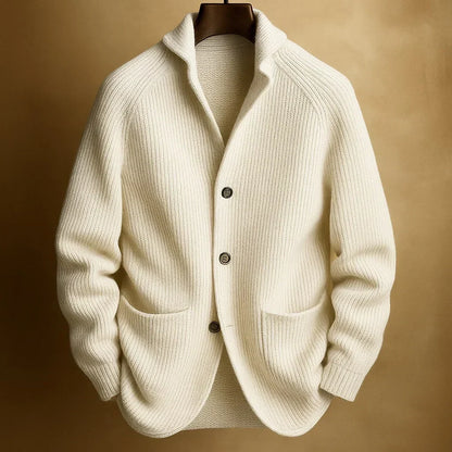 Cream ribbed knit cardigan with three buttons and patch pockets, hanging against a warm golden backdrop 2
