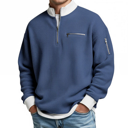 Front view of the blue waffle-knit jumper on a model, showing the half zip, chest zip pocket and zipped sleeve pocket. 3