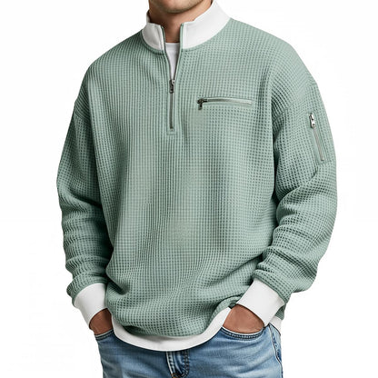 Front view of the pale green waffle-knit jumper on a model, with white collar, quarter zip and zipped pockets. 6