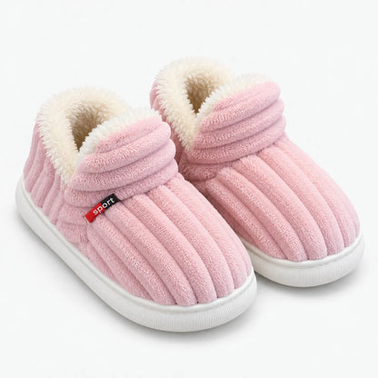 Pink plush winter slippers with soft faux fur lining, ribbed texture, cushioned ankle cuffs and white non-slip soles.