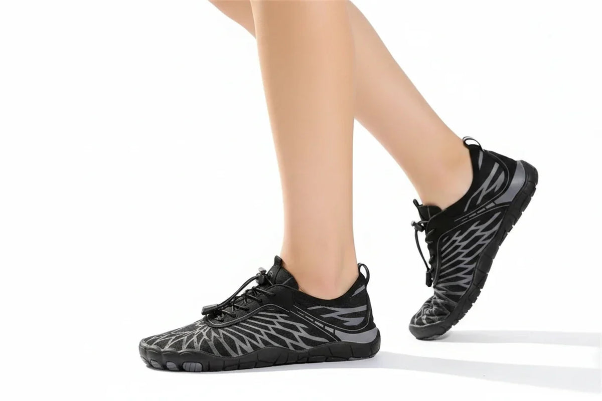 Side view of a model walking in black and grey barefoot shoes, showing the flexible low-profile sole. 20