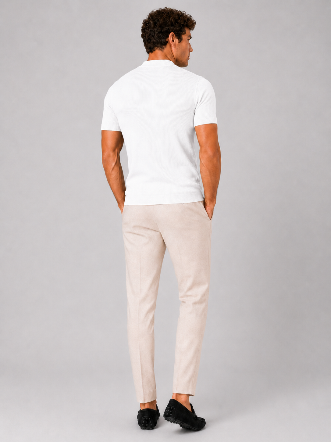 Back view of the white ribbed top worn with cream trousers and black loafers, model's hands in pockets. 14