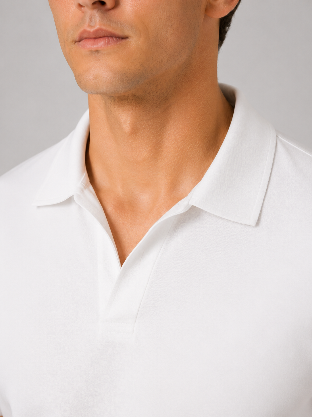 Close-up of the white polo's open V-neck collar and placket, showing the soft smooth fabric against a plain grey studio background. 2