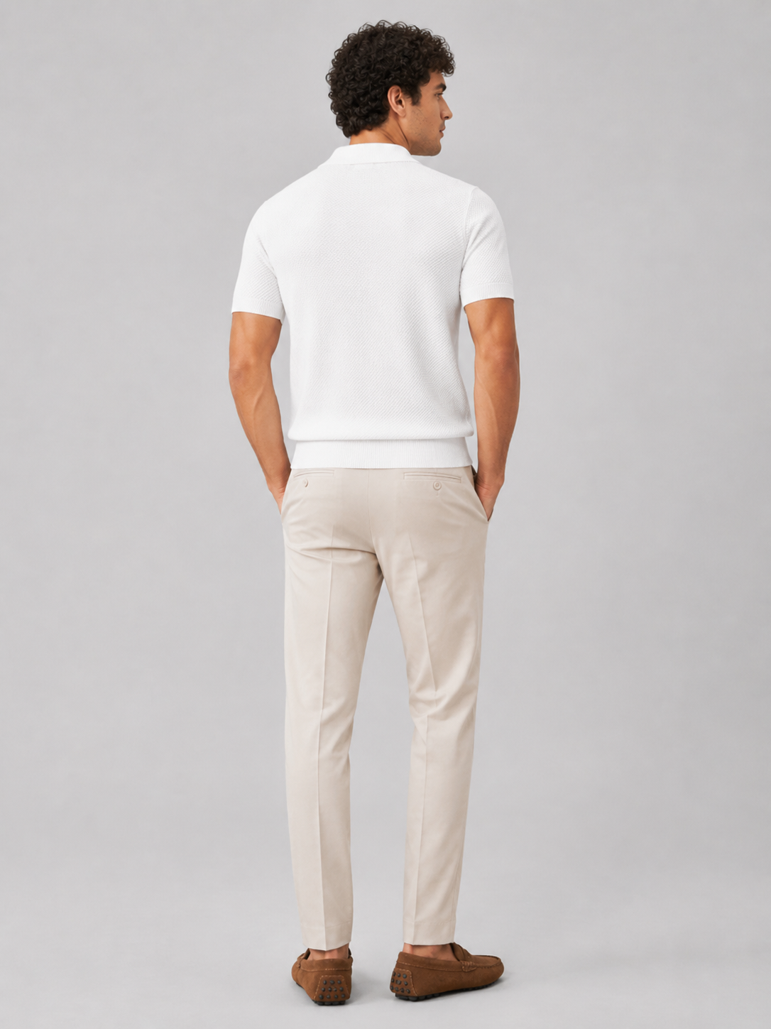 Back view of white knit polo on model with hands in pockets, light beige trousers and tan loafers 33