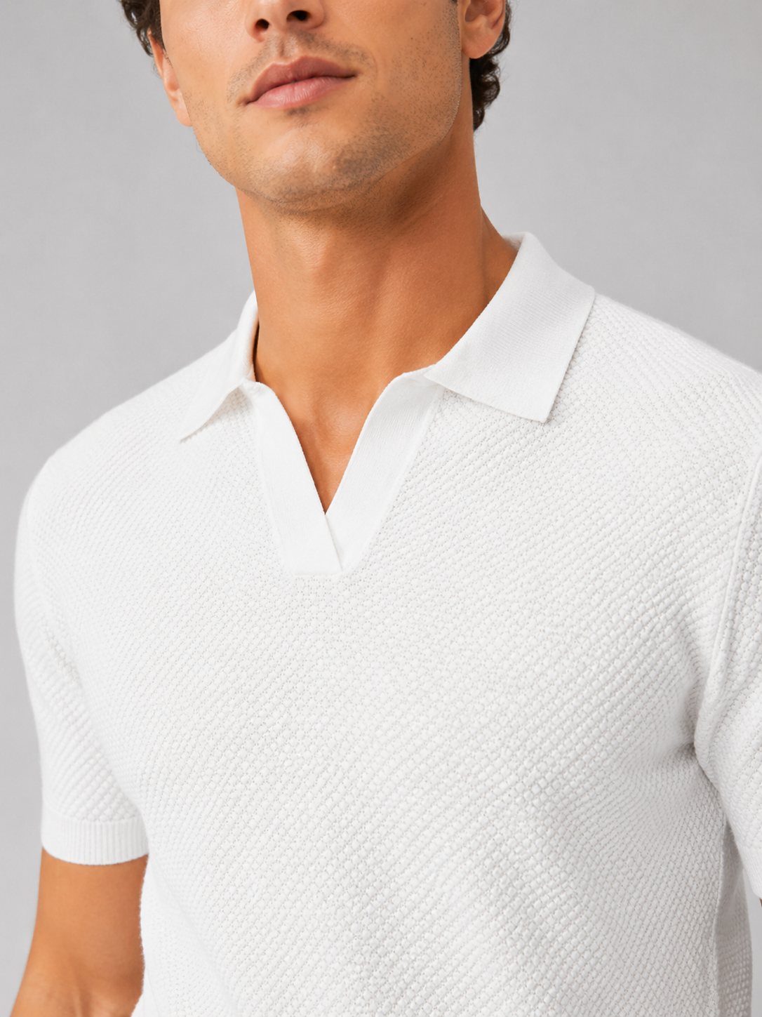 Close-up of white textured knit polo showing the open V-neck collar, honeycomb stitch and ribbed sleeve cuff 31