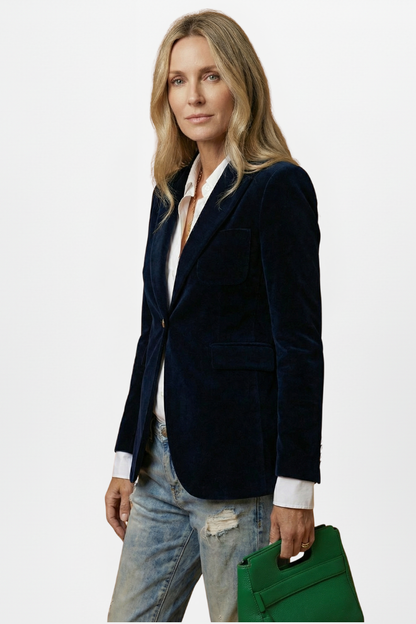 Side-angled view of the navy velvet blazer worn with a white shirt, model holding a green handbag 5