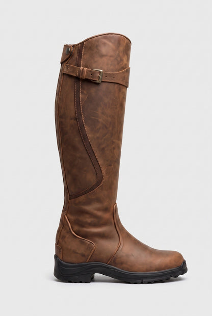 Side view of the knee-high boot in tan brown distressed leather with brass buckle and black lug sole 4