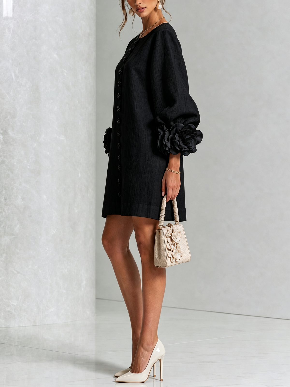 Black dress seen from the side on a model with cream heels and a small floral handbag, showing the puffed sleeve and rosette cuff. 22