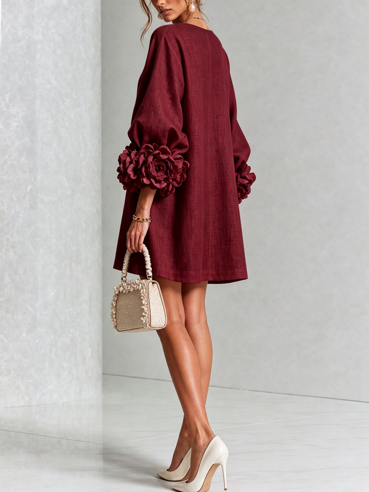 Back view of the burgundy mini dress, with a plain loose back, balloon sleeves and large floral cuffs, worn with cream heels. 37
