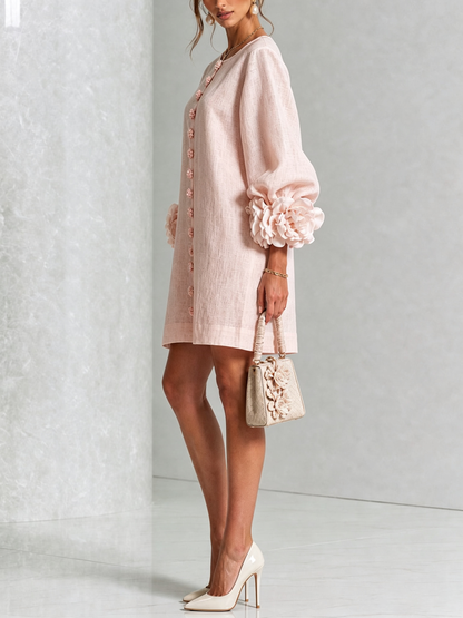 Pale pink dress in side view on a model holding a cream handbag, showing the balloon sleeve with its rosette cuff. 25
