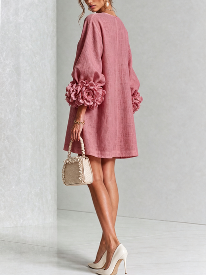 Back view of the dusky pink dress on a model looking over her shoulder, with large rosettes on the sleeves. 46