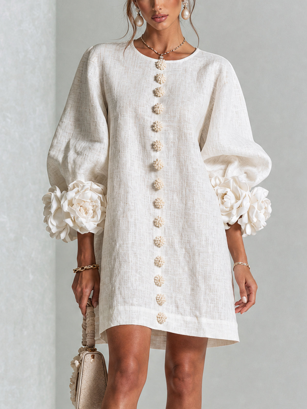 Model wearing the cream textured dress, front view, showing the row of floral buttons and large flower-trimmed volume sleeves. 1