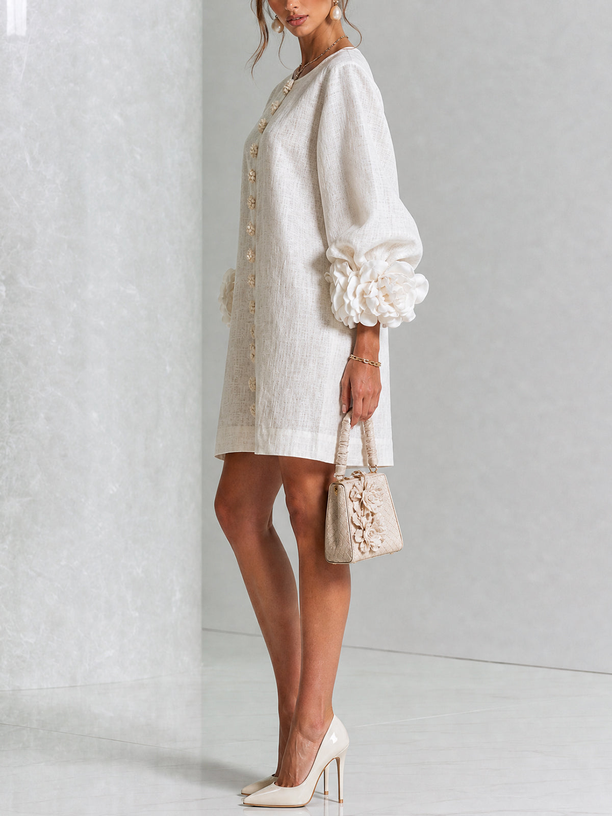 Side view of the cream dress on a model, showing the puffed sleeve with its oversized fabric rose cuff and flower buttons. 2
