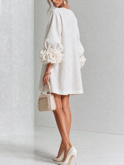 Back and side view of the cream dress in a studio, showing the plain back and rosette cuffs, with a small woven handbag. 14