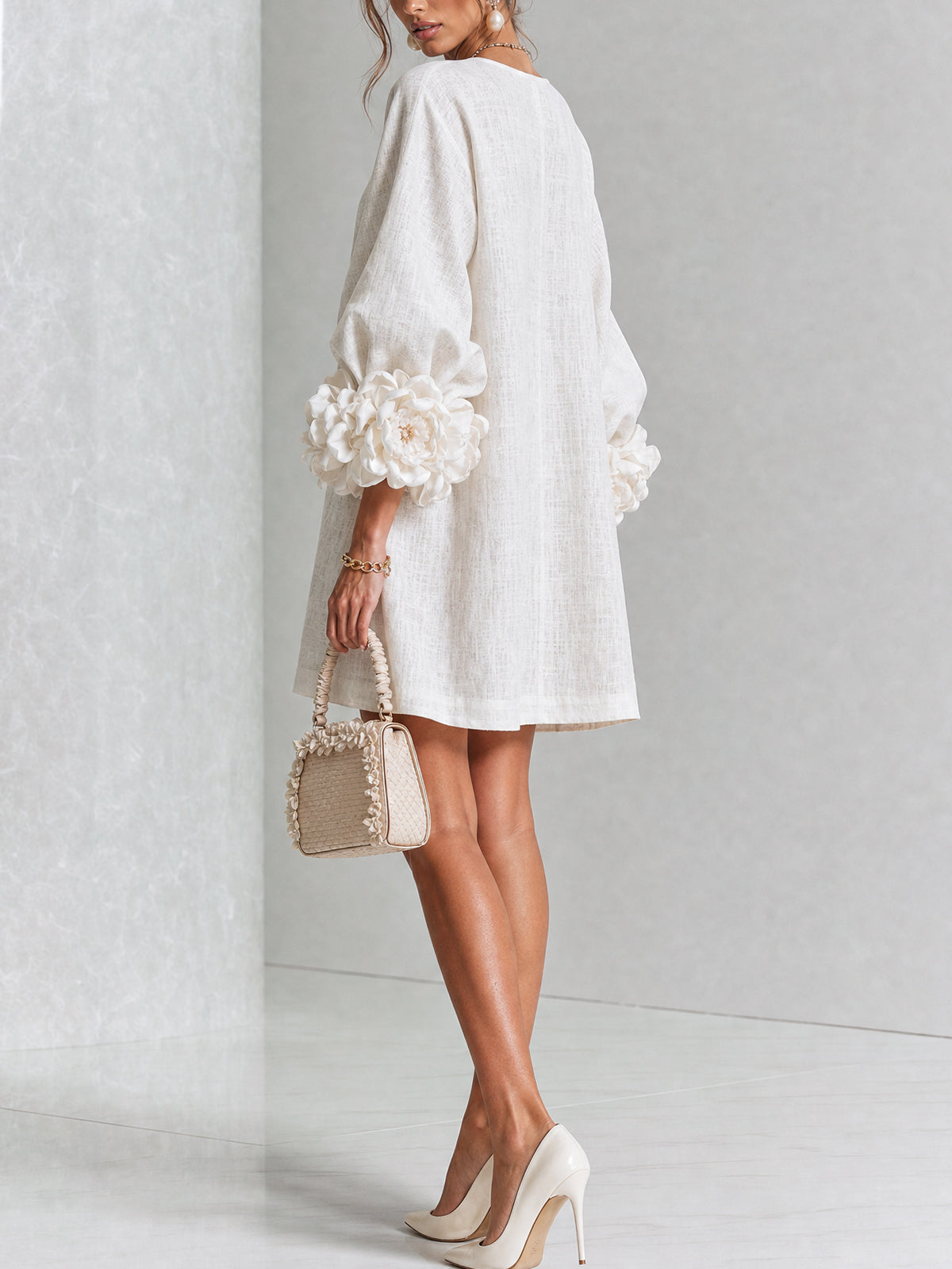 Back three-quarter view of the cream dress on a model, with loose straight back and large rose-shaped cuffs. 3