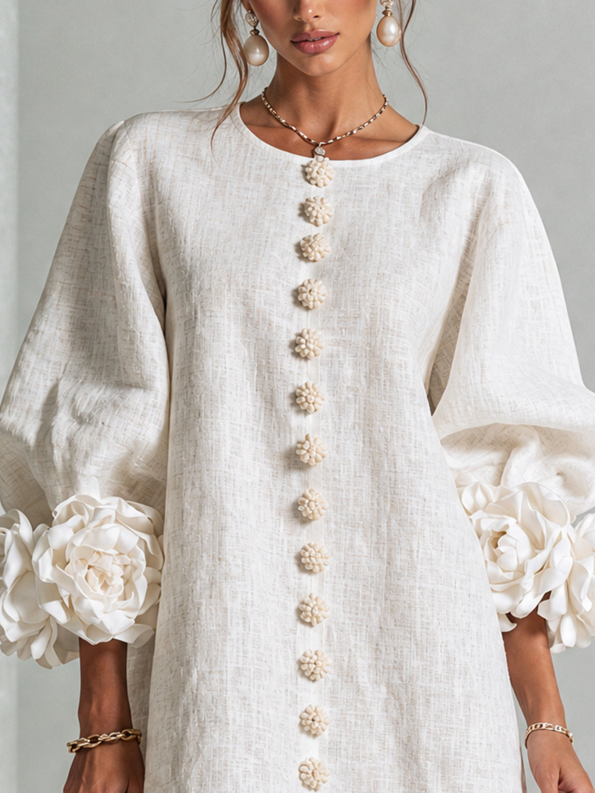 Close-up of the cream dress bodice, showing the round neckline, flower-shaped buttons and large rosette cuffs on puffed sleeves. 15
