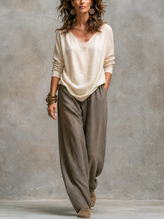 Model in the cream long-sleeved V-neck top and loose wide-leg taupe trousers, shown without the jacket against a plain wall. 2