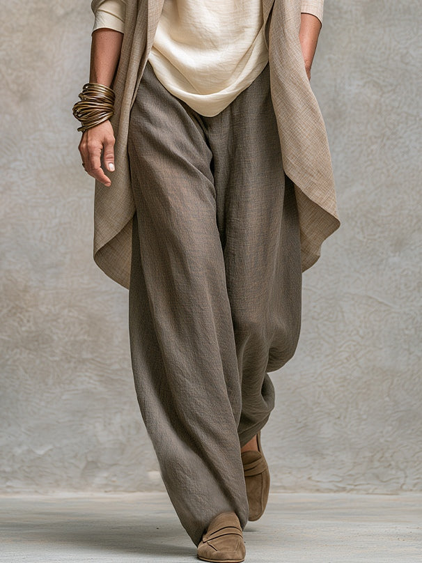 Detail of the relaxed wide-leg taupe trousers in a textured linen-look fabric, with the jacket hem and cream top visible above. 5