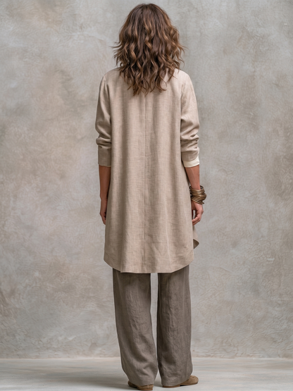 Back view of the long beige jacket with its centre back seam and curved hem, worn over taupe wide-leg trousers. 6