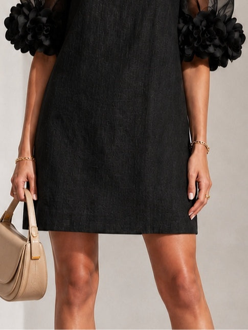 Cropped view of the dress's skirt and sleeve cuffs, showing the subtle textured weave and straight hem, with a beige bag in hand. 6