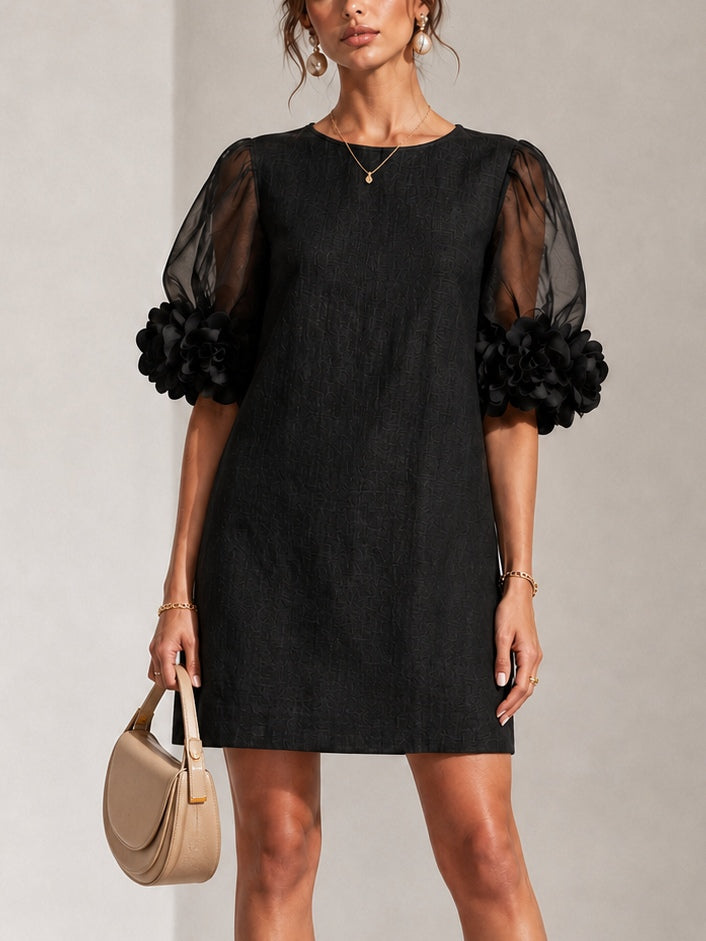 Model facing forward in the black textured shift dress, showing sheer puffed sleeves with dark floral cuffs, holding a beige saddle bag. 1