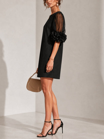 Side view of the black dress on a model in strappy heels, showing the sheer sleeve and the ruffled flower cuff in profile. 2