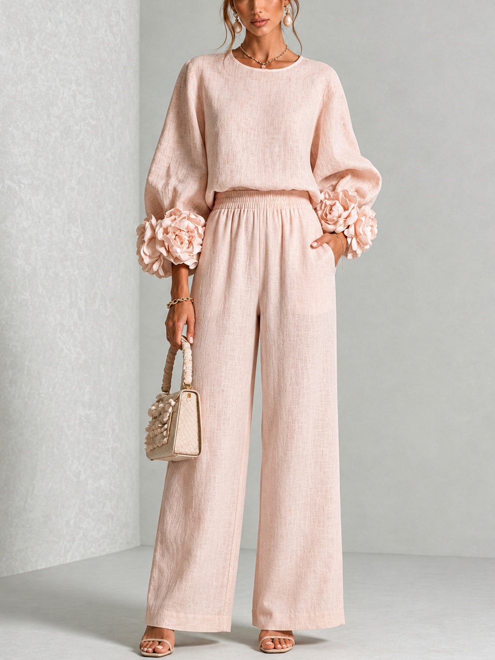 Model standing front-on in the blush pink set, flower-trimmed sleeves, holding a cream woven handbag 1
