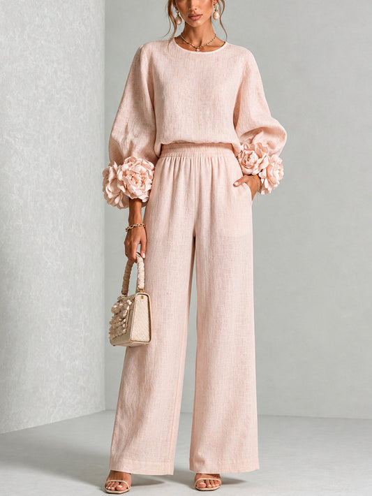 Model standing front-on in the blush pink set, flower-trimmed sleeves, holding a cream woven handbag 1
