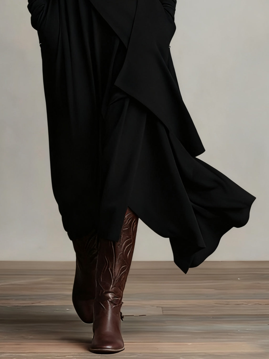 Close-up of the black skirt's flowing asymmetric draped layers above embossed brown leather boots 8