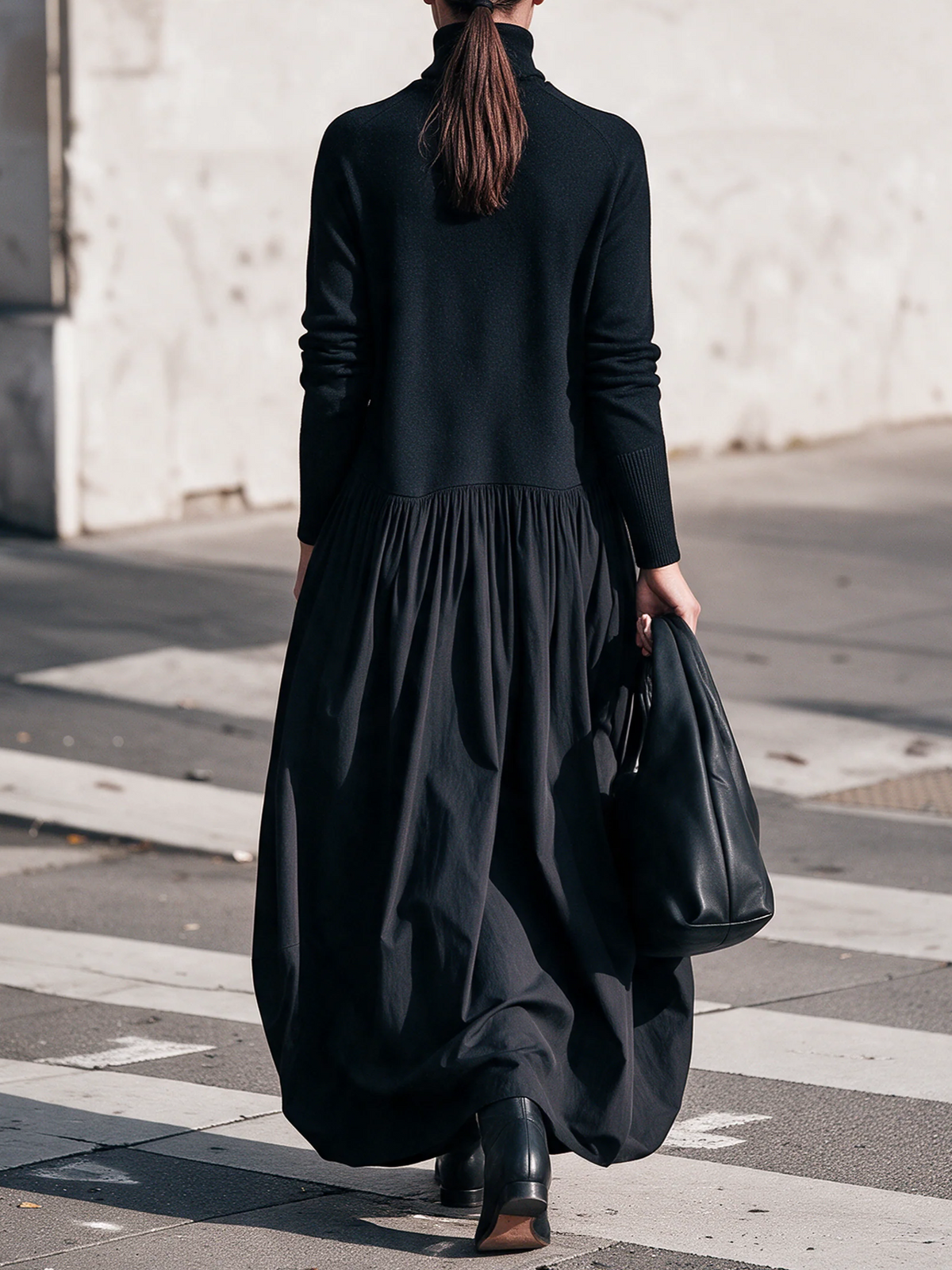 Back view of the black dress on a model with a ponytail, walking away holding a bag 3