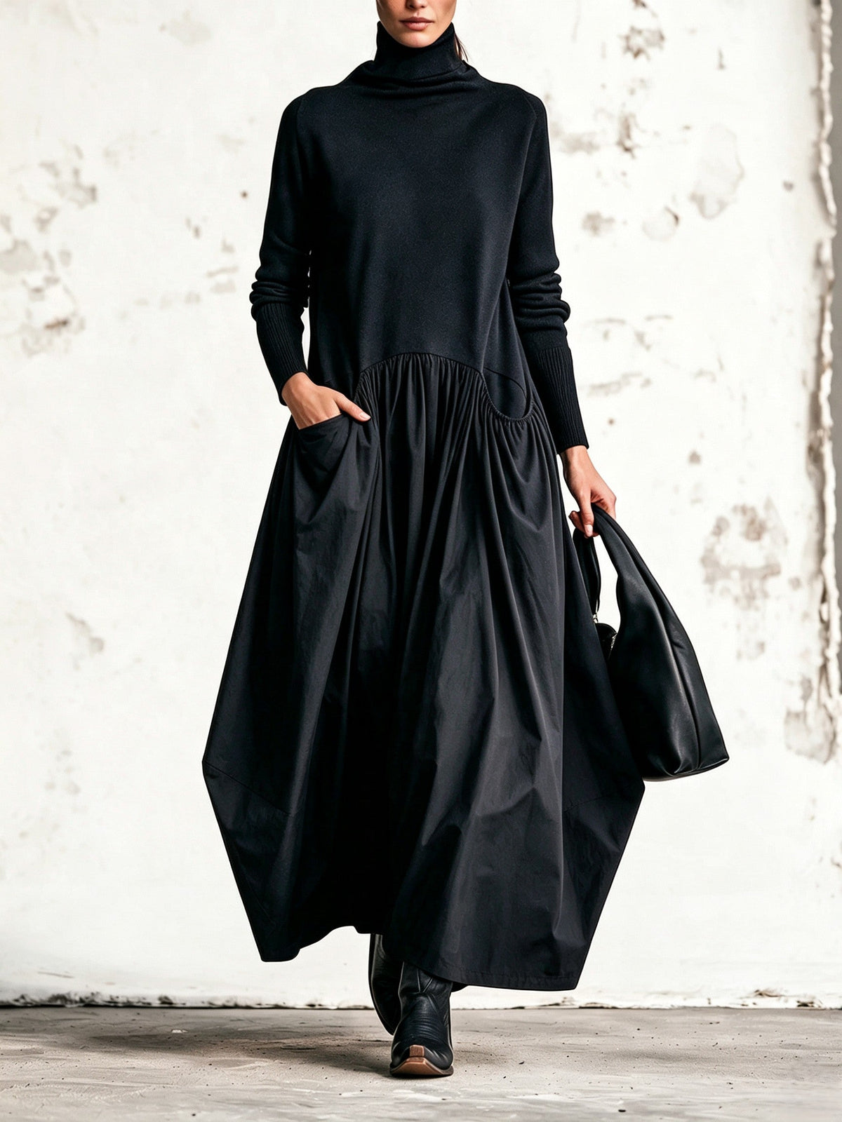 Model walking in the black dress with one hand in a gathered side pocket, holding a black bag 1