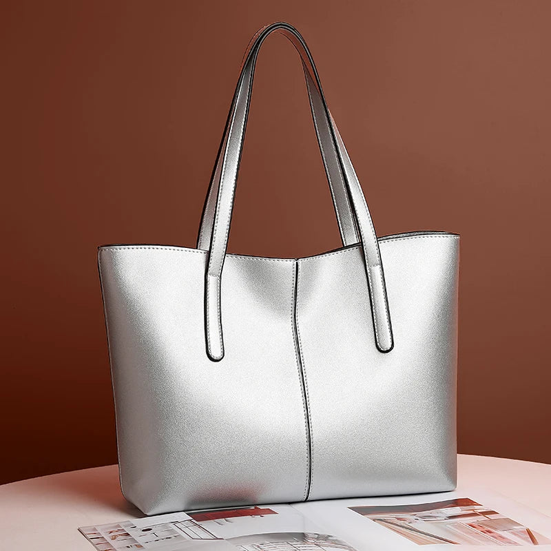 Silver tote bag angled on a white table against a brown wall, with a magazine beneath 2